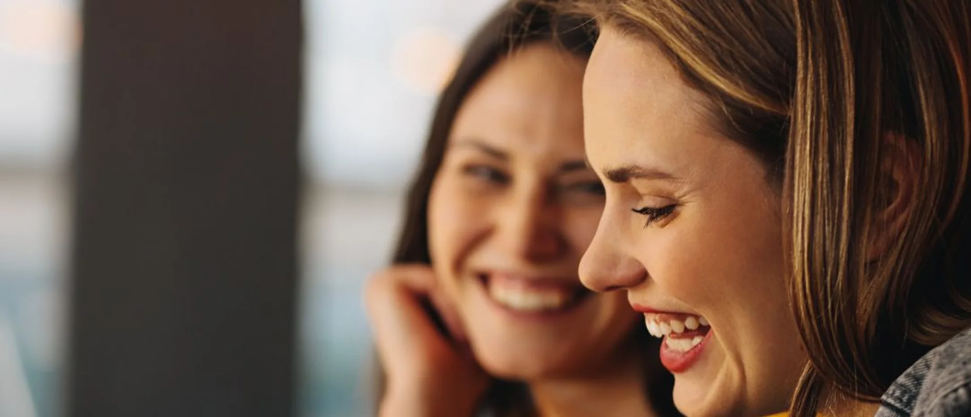 Two friends laughing together over a phone in a warm café.