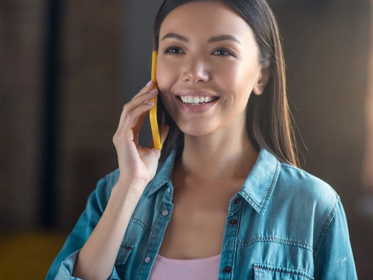 A relaxed professional in denim smiling during a call, papers in hand.